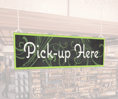 Natural Collection's wayfingding hanging department sign that has "Pick-up Here," digitially printed in white text and on PVC